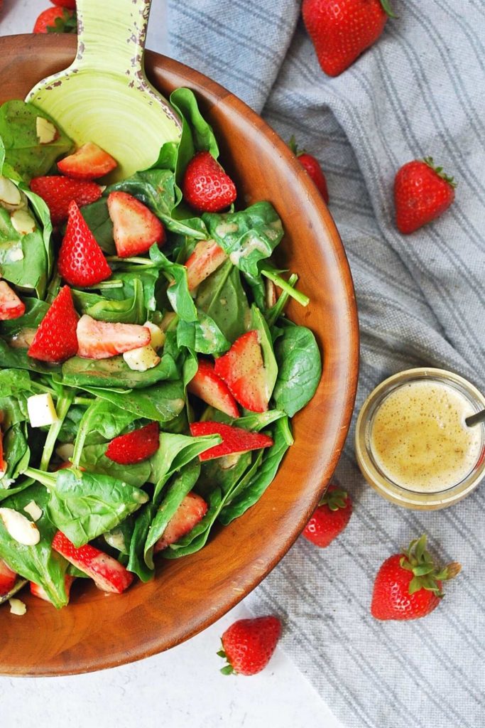 overhead photo of a bowl of strawberry spinach salad with berries and dressing on the side