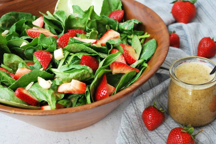 side view of a wooden bowl filled with strawberry spinach salad with fresh berries around the bowl and dressing on the side