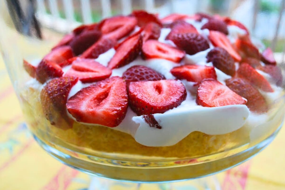 the first layer of a tres leche trifle with strawberries and whipped topping in a trifle bowl