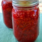 two jars of strawberry jam on a green tablecloth