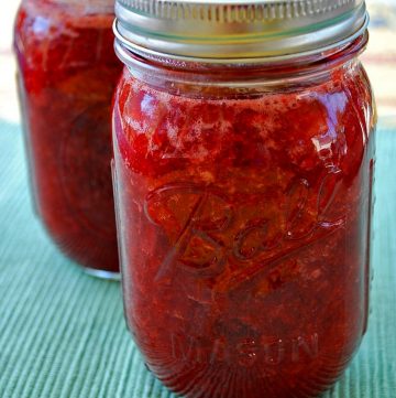 two jars of strawberry jam on a green tablecloth