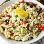 close up of greek chicken pasta salad in a large bowl garnished with lemon and herbs
