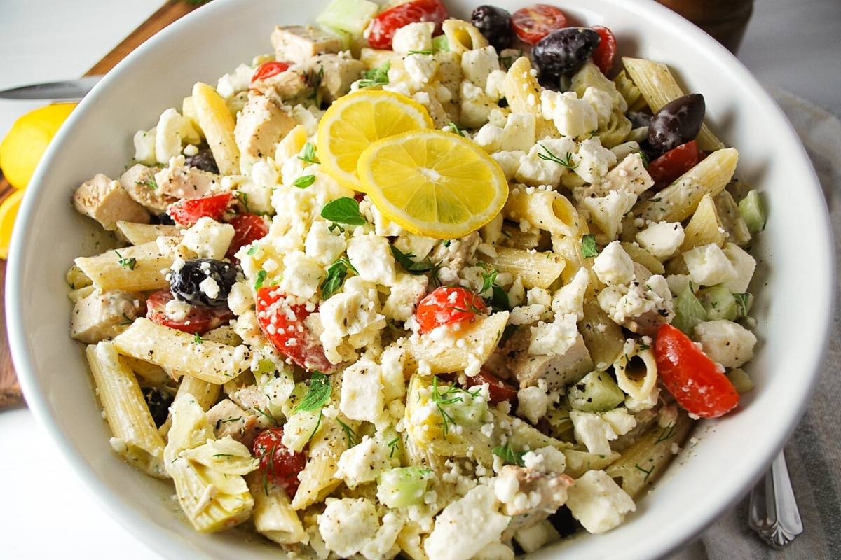 close up of a bowl of Greek chicken salad topped with slices of lemon
