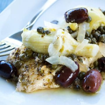 close up of Mediterranean halibut with olives, artichokes, onions, capers, and spices on a plate with a fork