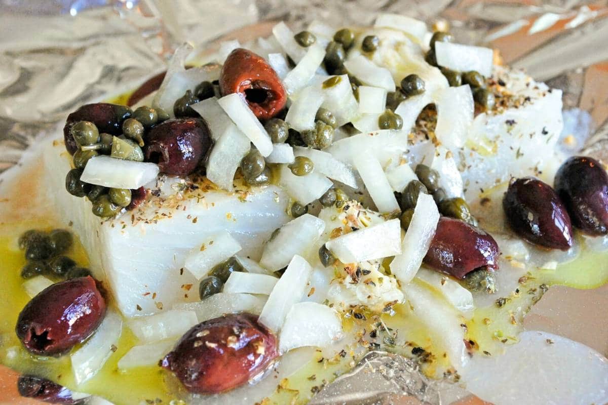 halibut fillet topped with olives, onions, and capers and olive oil on top of foil
