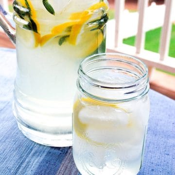 close up of a glass of lemonade next to a pitcher of lemonade on a patio table