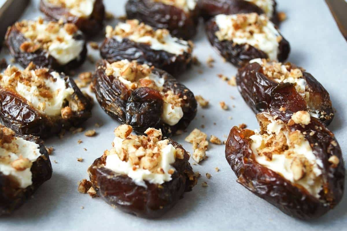 dates stuffed with mascarpone cheese and sprinkled with pecans on a baking sheet