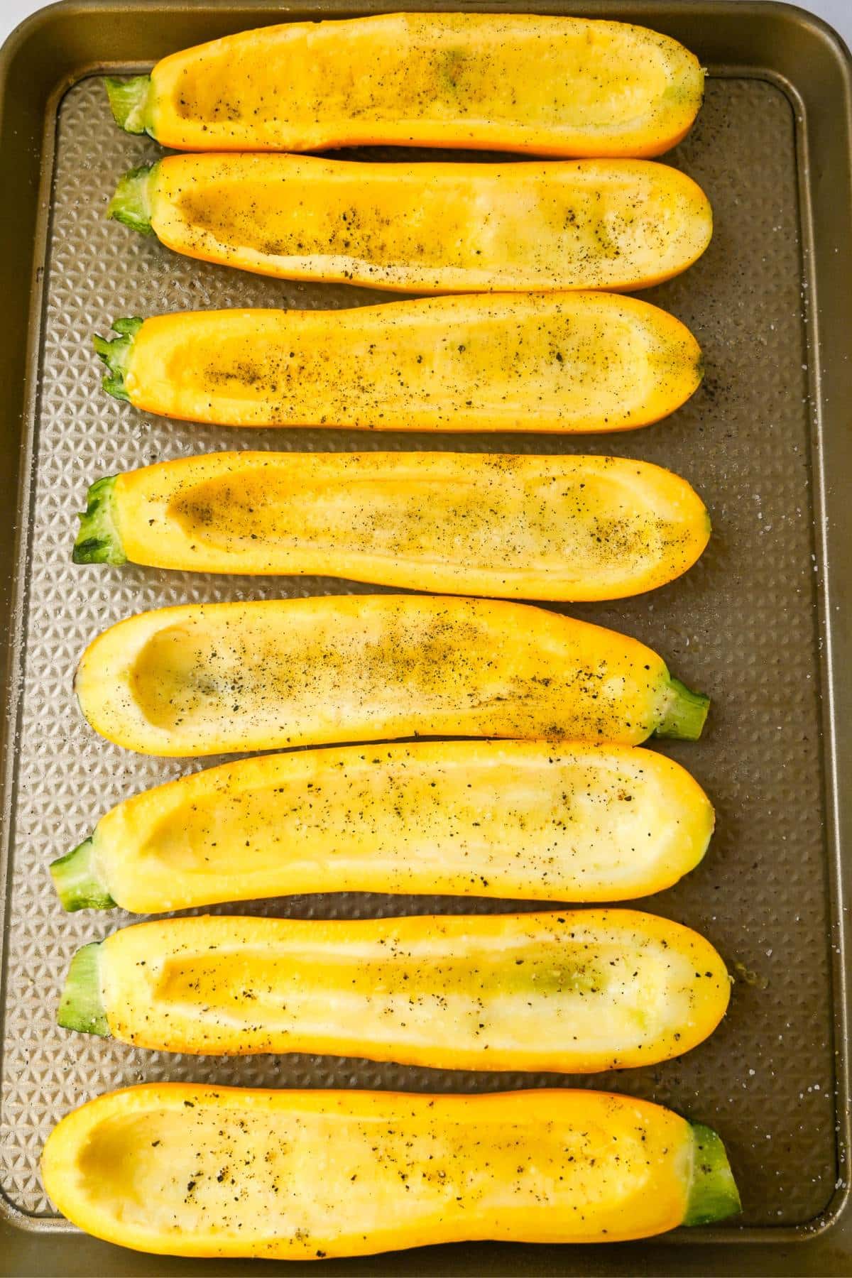 hollowed out squash halves on a baking sheet sprinkled with salt and pepper