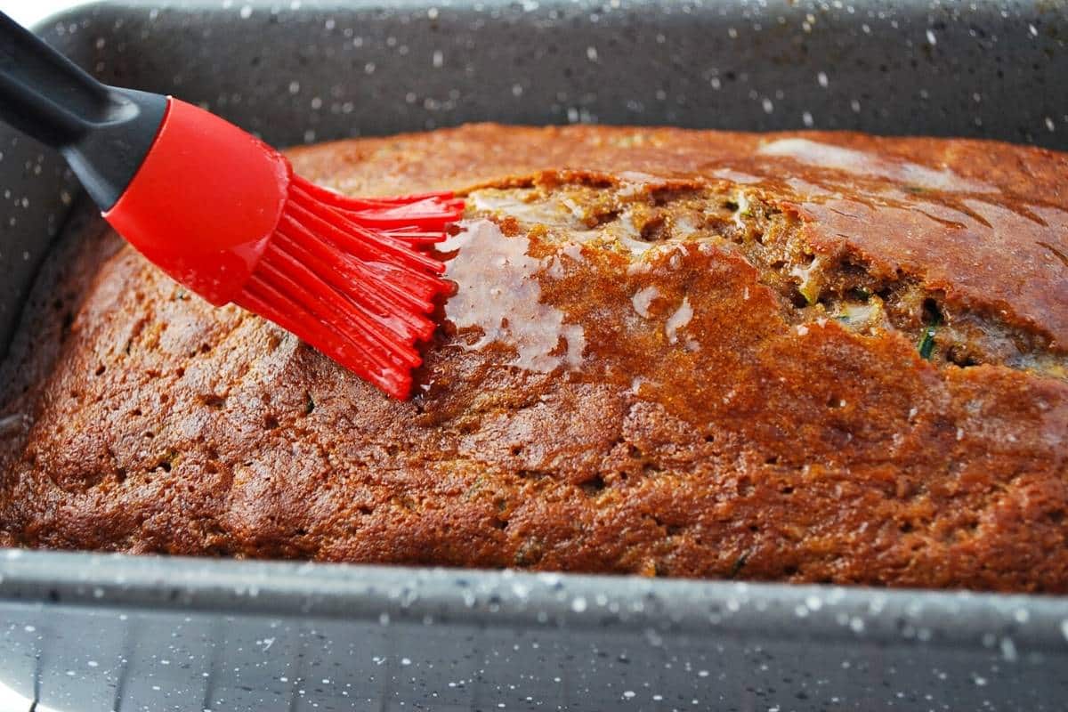 basting the top of a zucchini bread loaf with melted butter