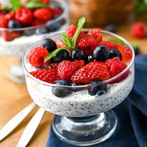 close up photo of a chia seed parfait with blueberries, raspberries, and strawberries on top with spoons next to it