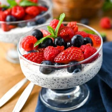 close up photo of a chia seed parfait with blueberries, raspberries, and strawberries on top with spoons next to it