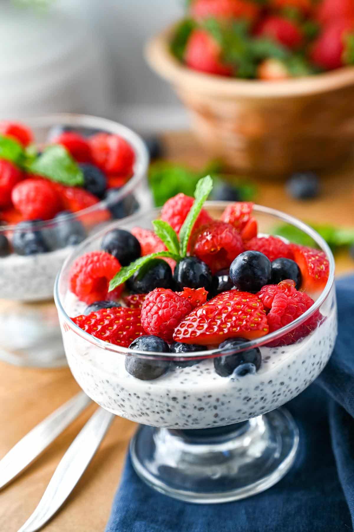 two chia puddings made with yogurt and milk with fresh berries on top and a bowl of berries behind them