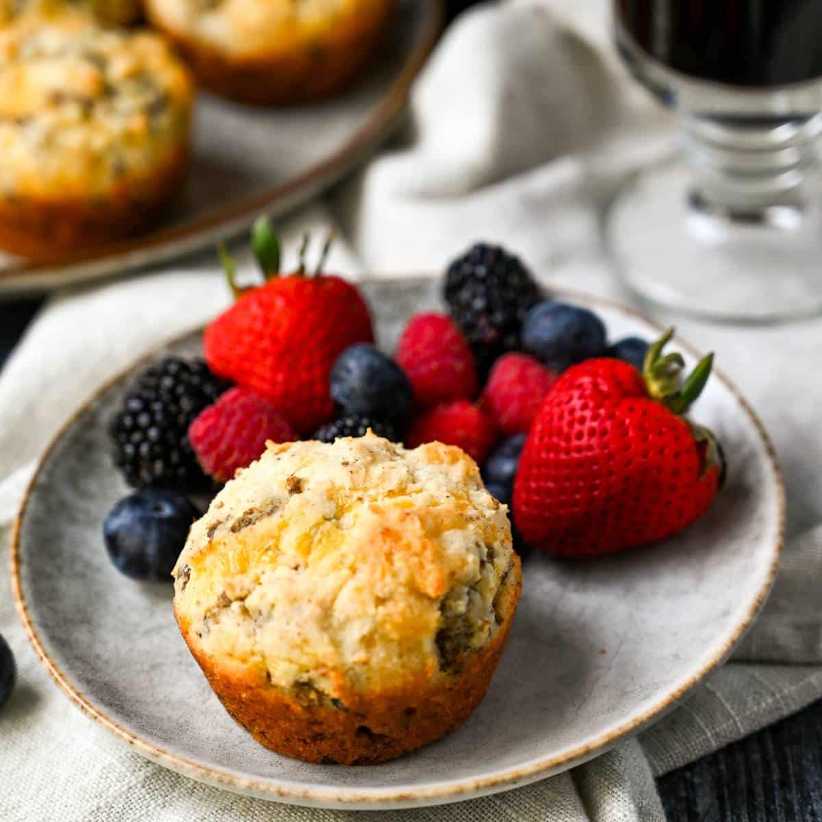 a sausage and cheese muffin on a gray plate with strawberries, blueberries, and raspberries
