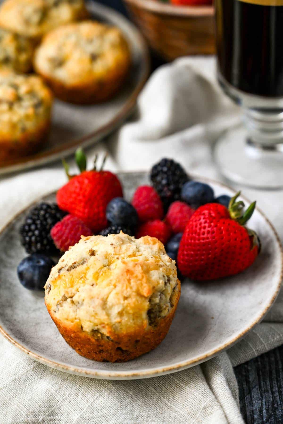 a sausage and cheese muffin on a gray plate with strawberries, blueberries, and raspberries with a cup of black coffee