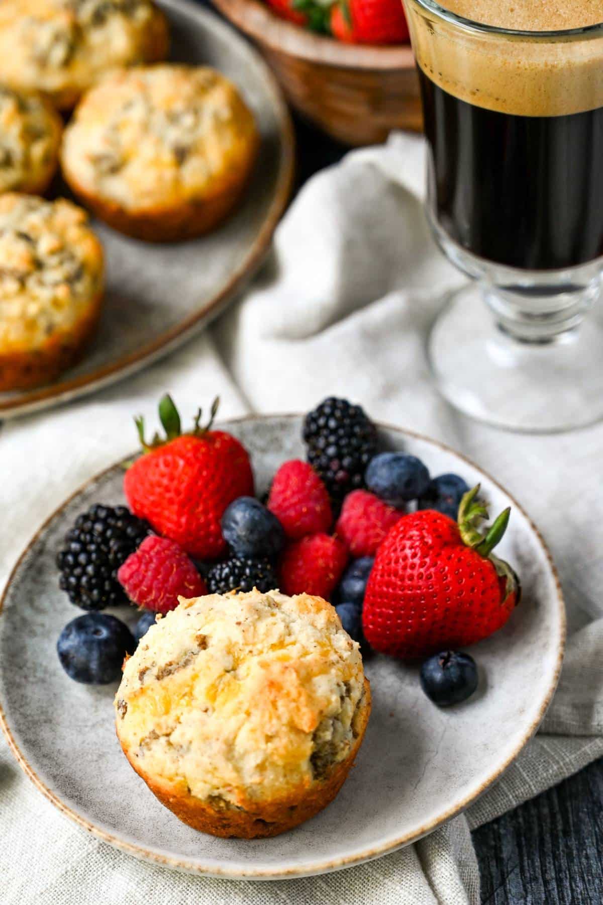 sausage and cheddar muffins on a plate with berries with a plate of muffins and coffee in the background