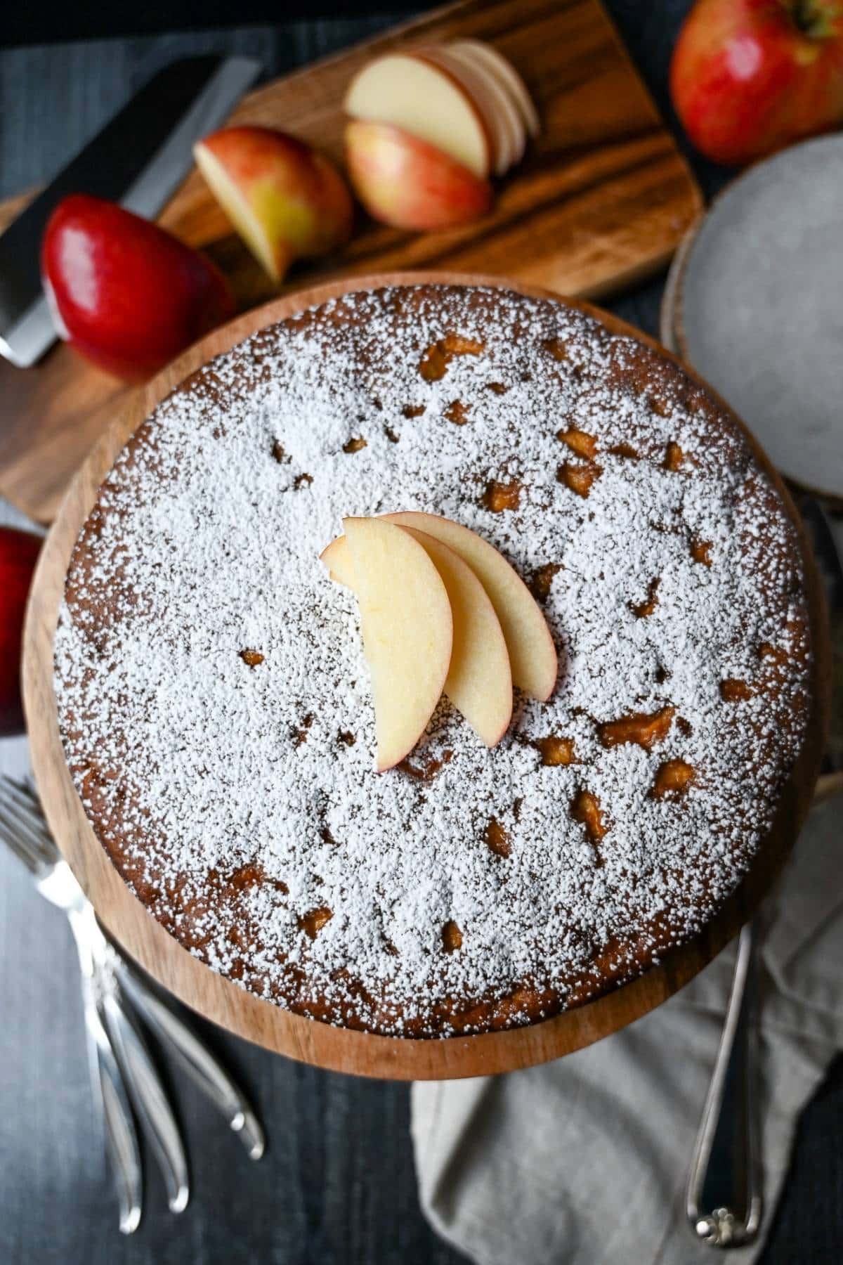 a whole spice cake with powdered sugar and sliced apples 