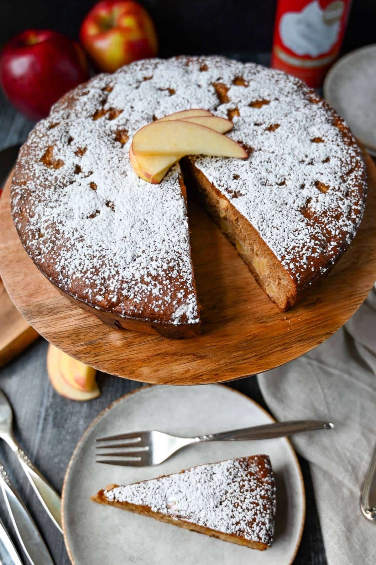 a slice cut out of a spice cake with a cake on a cake stand behind it