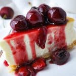 a close up slice of keto lemon cheesecake covered in cherry compote with a fork on a plate