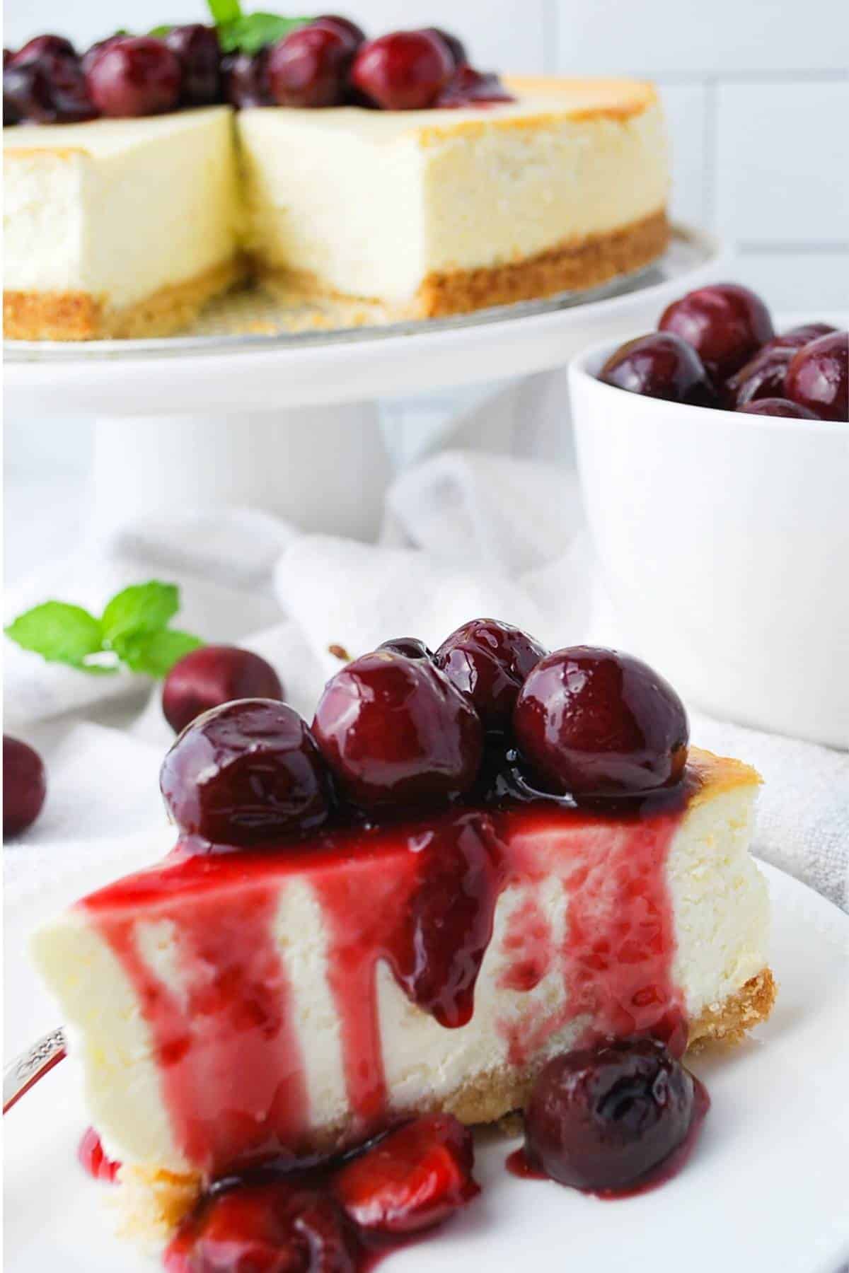 a slice of lemon keto cheesecake with cherry compote on top with a sliced cheesecake on a cake stand in the background