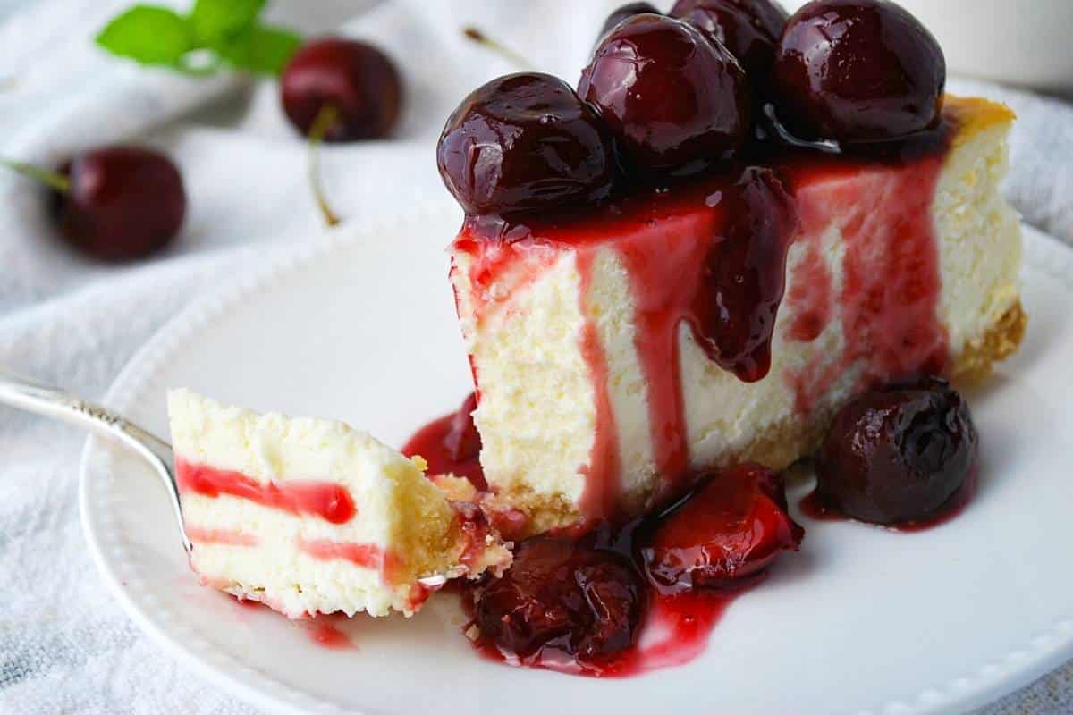 a slice of cheesecake with cherry compote dripping down the sides with a fork sliced bite