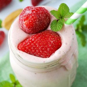 close up of a strawberry peanut butter banana smoothie in a mason jar dripping over the sides with a green striped straw
