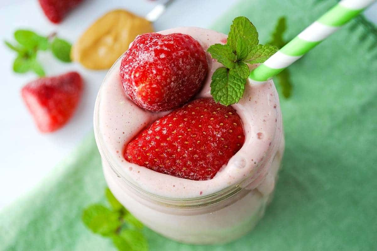 close up of a strawberry smoothie with frozen strawberries and peanut butter in the background