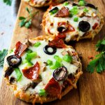 2 open-faced English muffin pizzas loaded with toppings on a serving board
