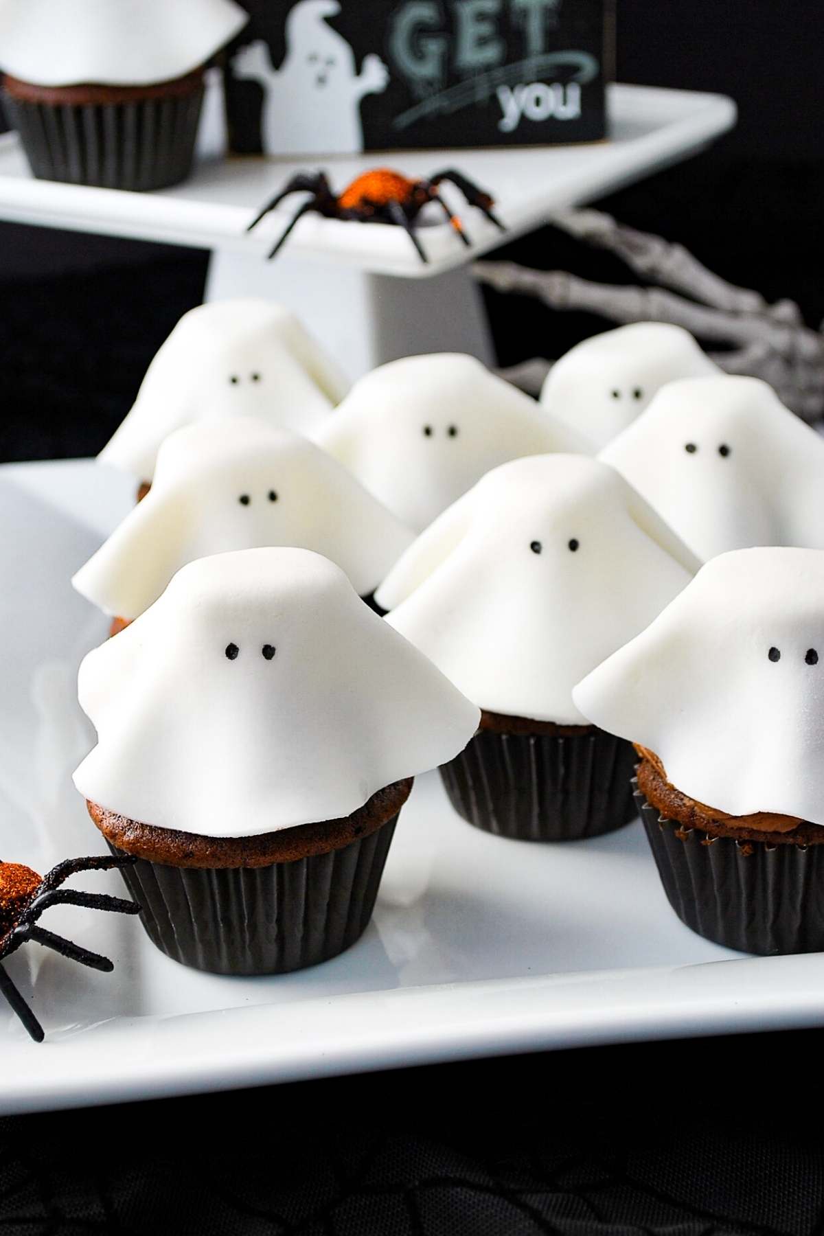 fondant ghost cupcakes on a white platter with plastic spiders