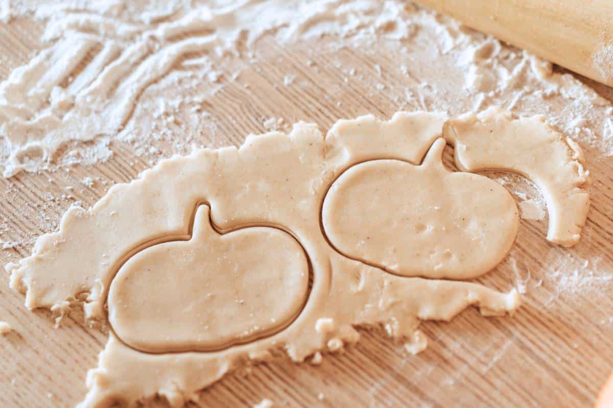cutting out pumpkin shape cookies from rolled out dough