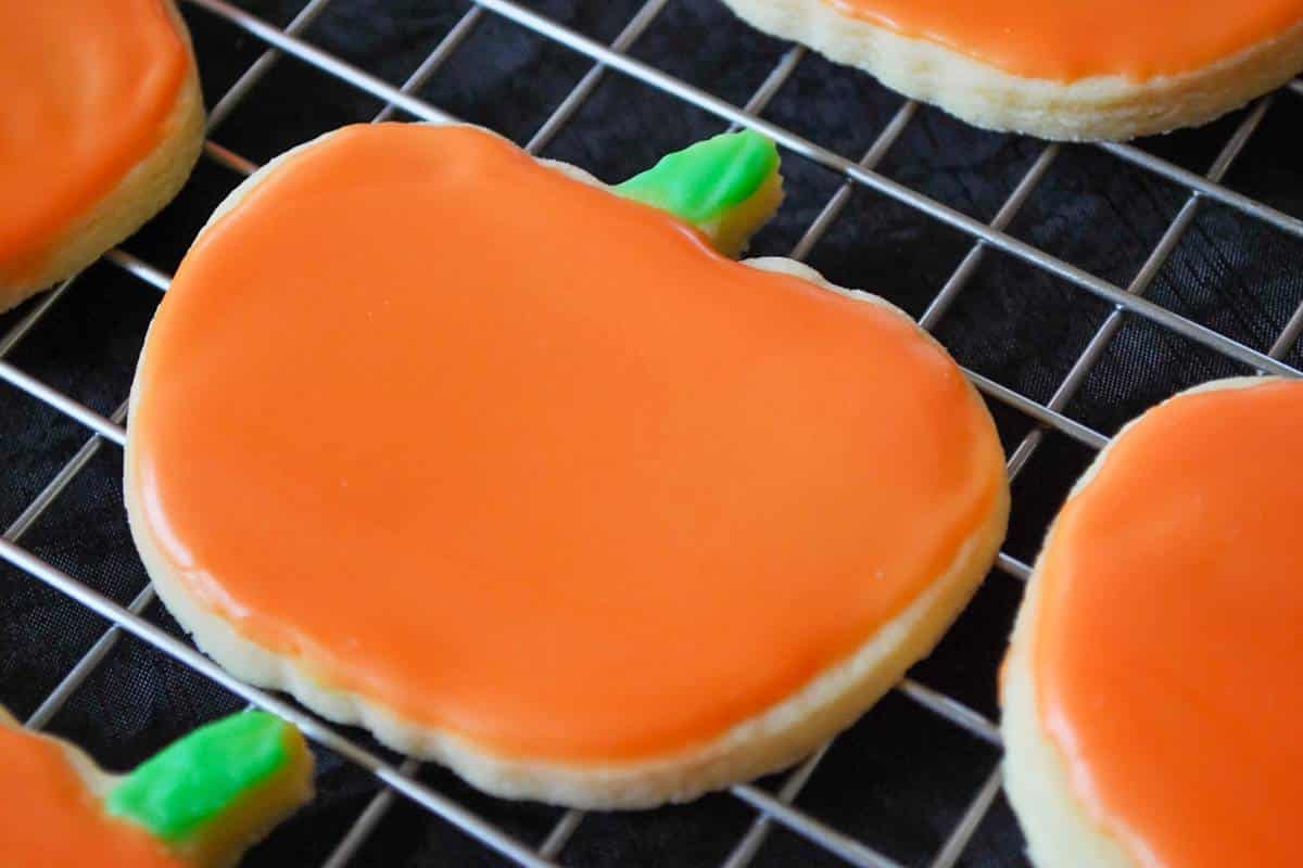 close up of a pumpkin frosted sugar cookie on a rack with colored icing