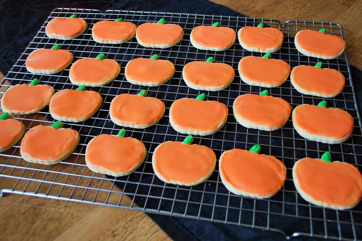 frosted pumpkin shaped cookies with orange and green tinted royal icing on a cookie rack