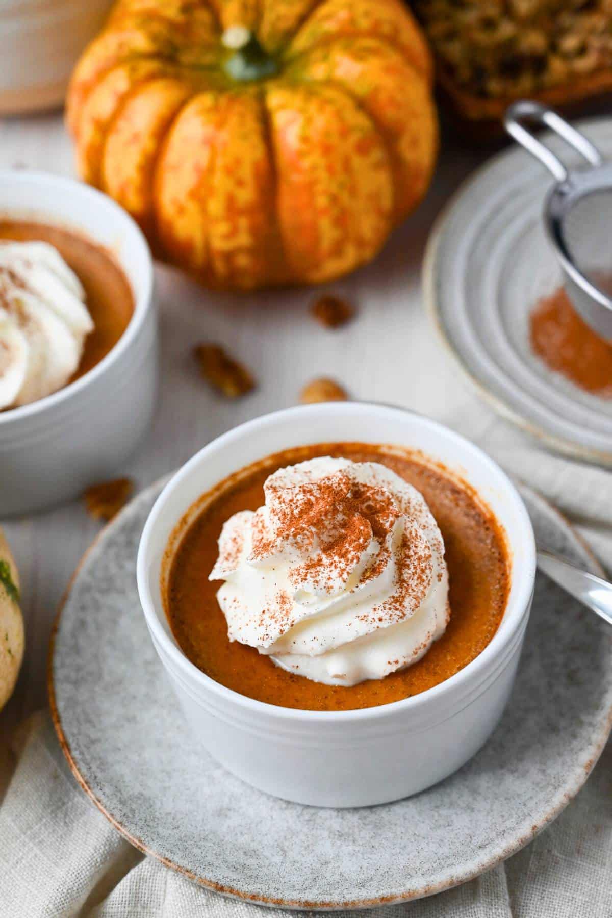 pumpkin baked custard in a ramekin with whipped cream and cinnamon and pumpkins in the background
