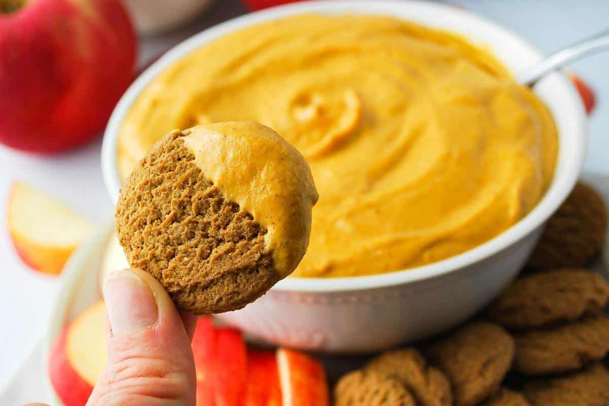 A gingersnap dipped in pumpkin dip on a platter of sliced apples and gingersnaps
