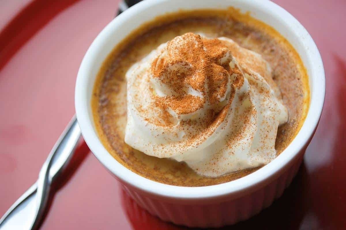 pumpkin pie custard served in a ramekin with whipped cream and a dusting of cinnamon with a spoon on the side