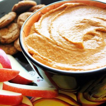 close up of pumpkin dip in a black bowl with apple slices and gingersnaps around it