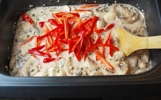 Chicken coconut curry soup in a slow cooker with red peppers on top