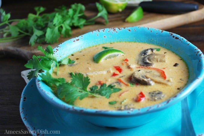 Close up photo of chicken curry soup in a blue bowl with fresh herbs