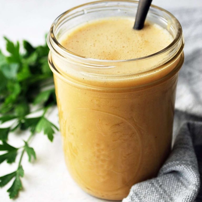 close up of a jar of honey mustard vinaigrette dressing with parsley behind it