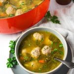bowl of meatball soup with spoon and fresh herbs sprinkled on top