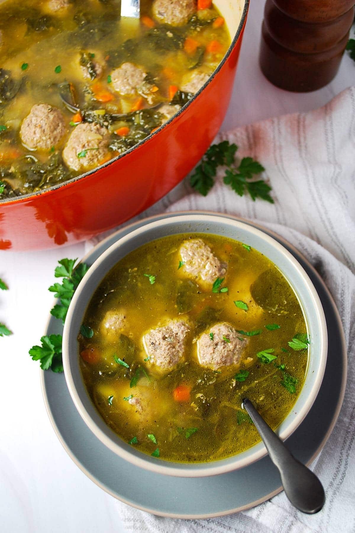 photo of a bowl of paleo meatball soup with a spoon with pot of soup in the background