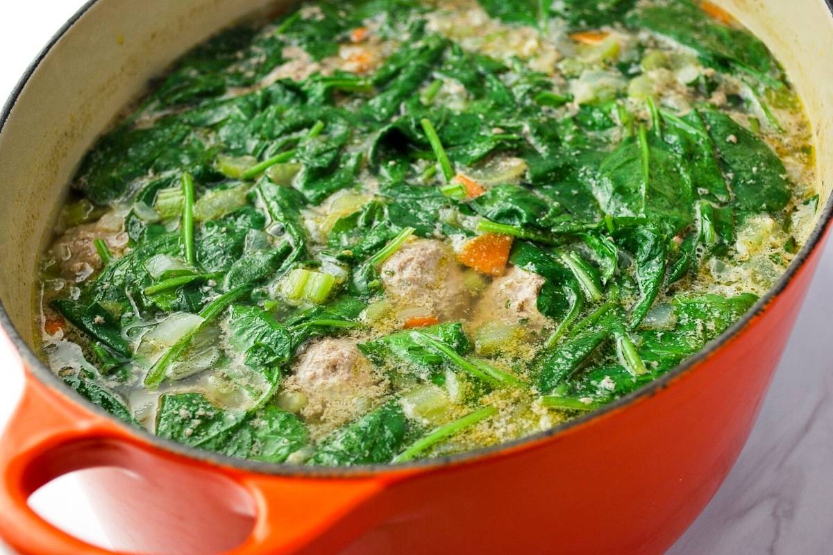 meatball soup with spinach simmering in an orange dutch oven