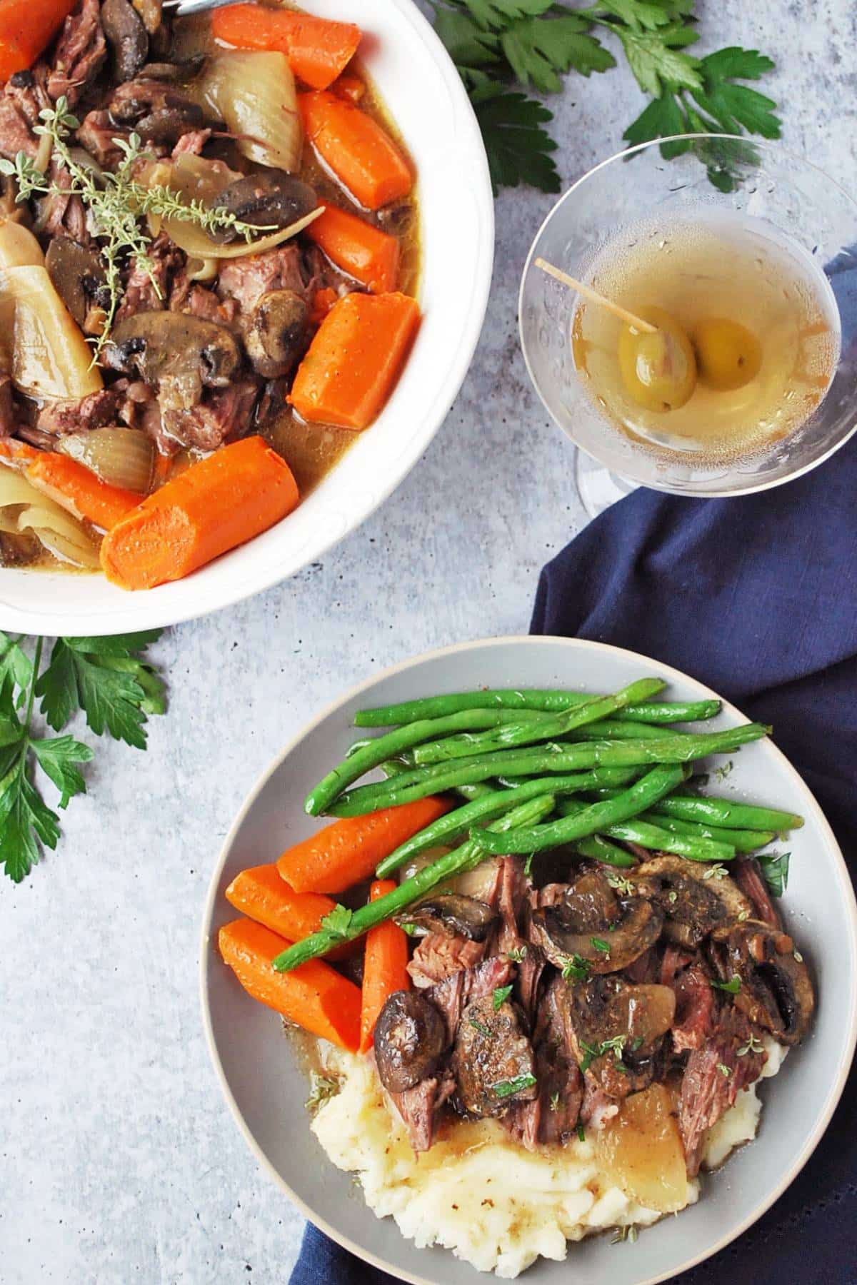 overhead photo of pot roast and carrots in a serving dish with pot roast on a plate with mashed potatoes, green beans, and carrots