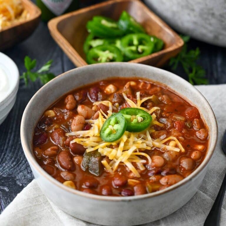 close up of a bowl of chili with melting cheese and jalapenos with a bowl of fresh jalapenos