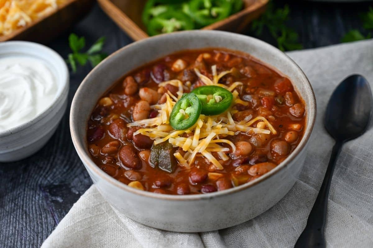 close up of a bowl of veggie bean chili with cheddar cheese and jalapenos