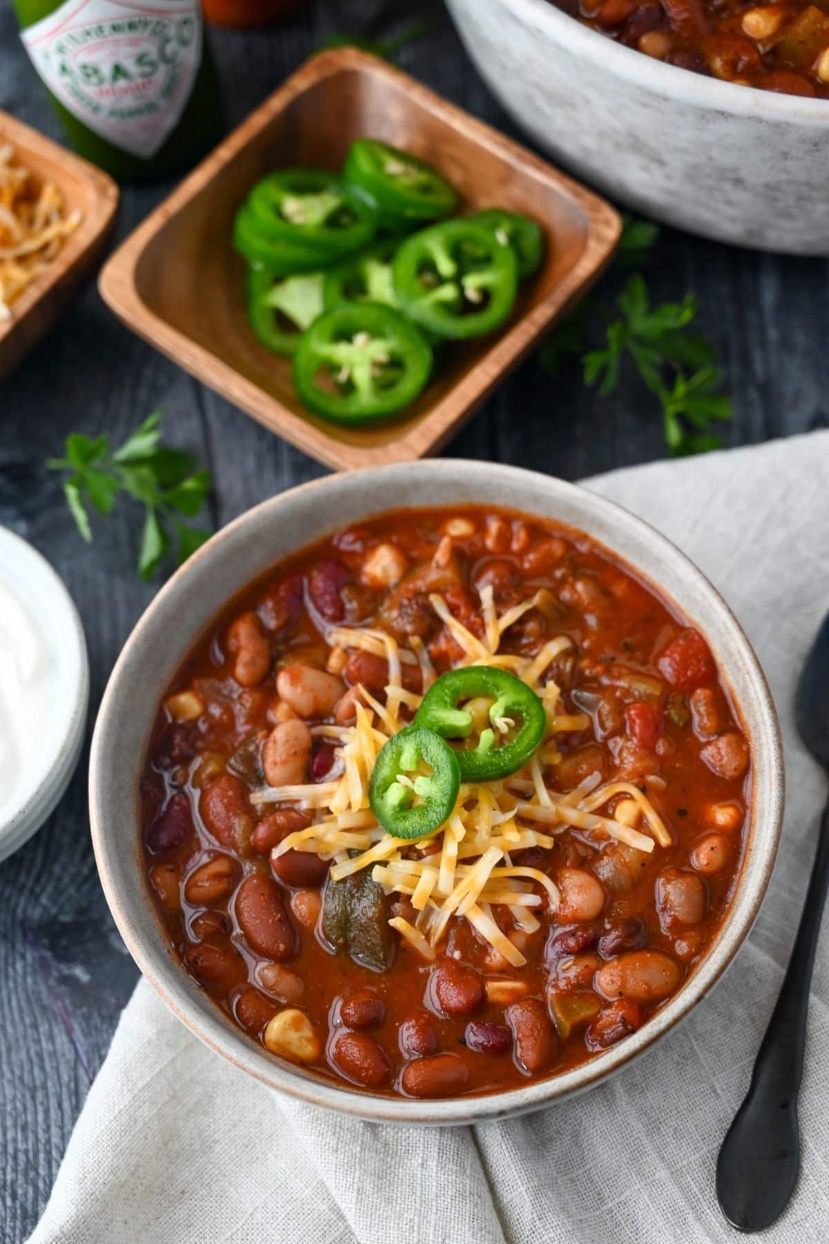 looking down at a bowl of chili with a napkin and spoon with shredded cheese and fresh jalapeno peppers