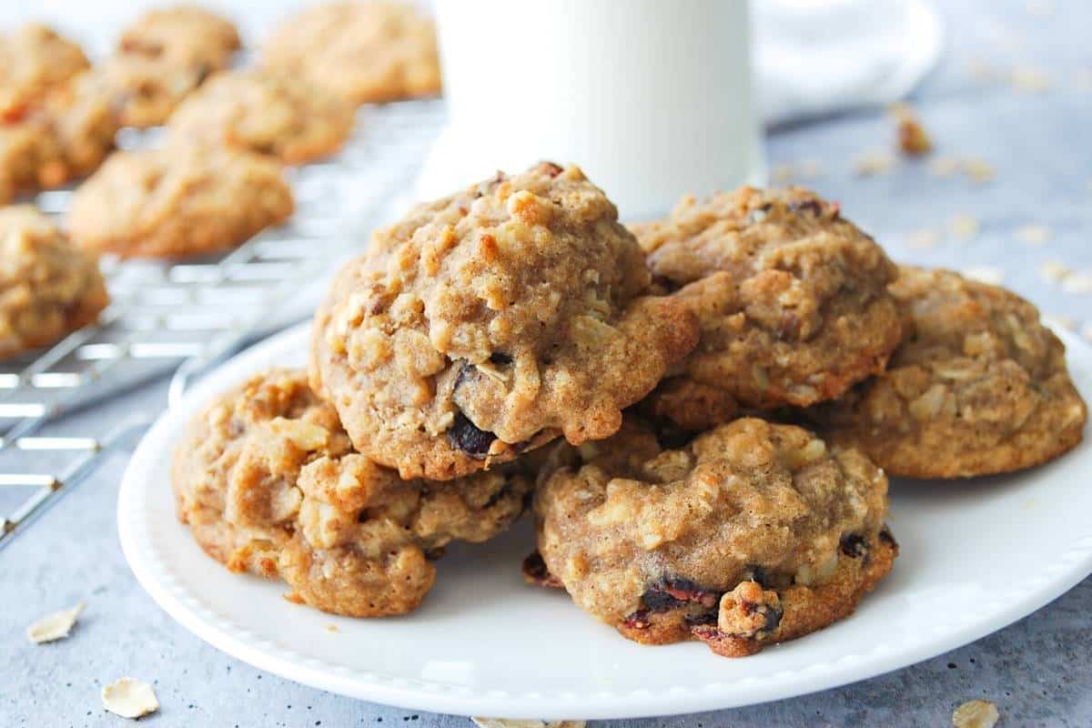 a plate of gluten free oatmeal cranberry cookies with a glass of milk and cookies in the background