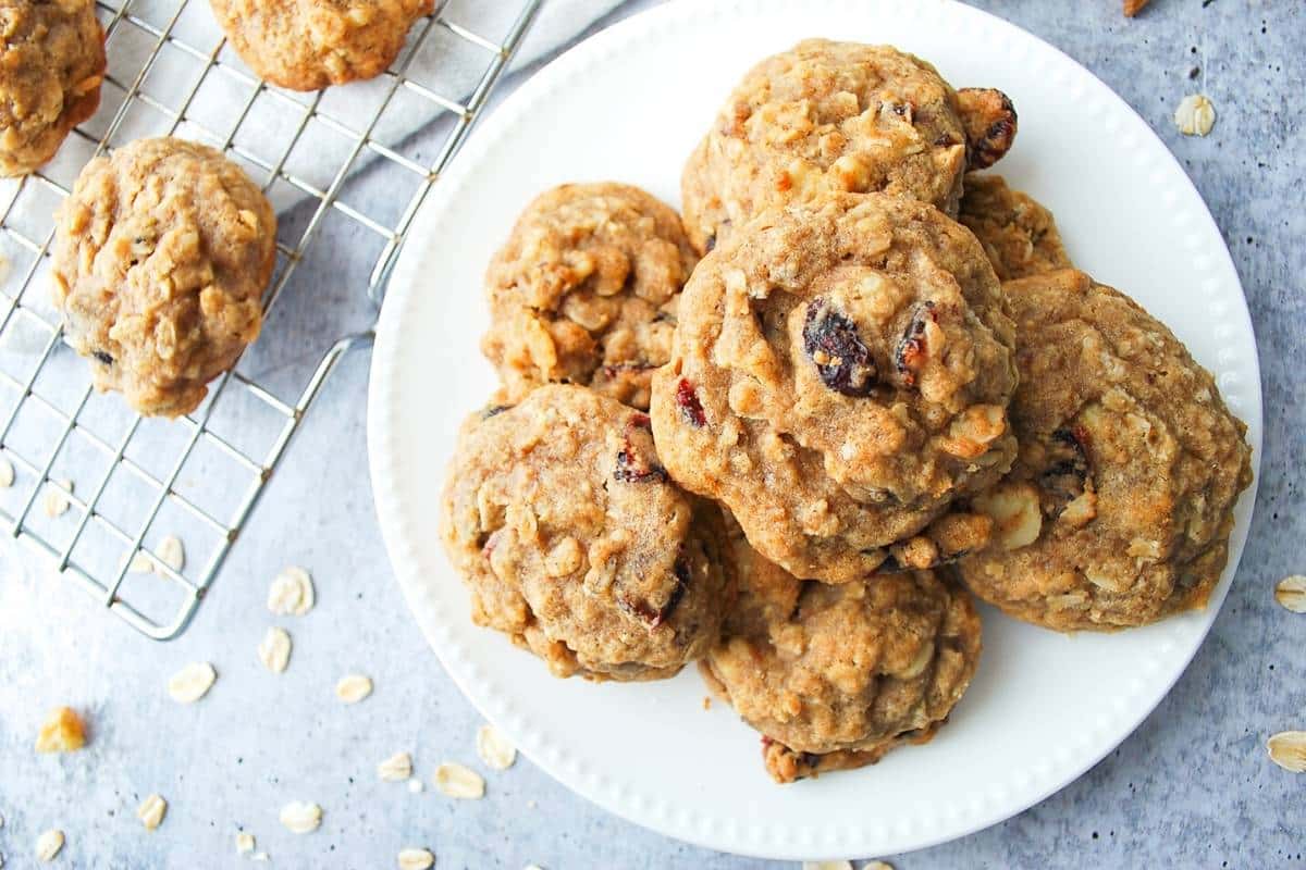 oatmeal cookies on a white plate with cookies cooling behind it