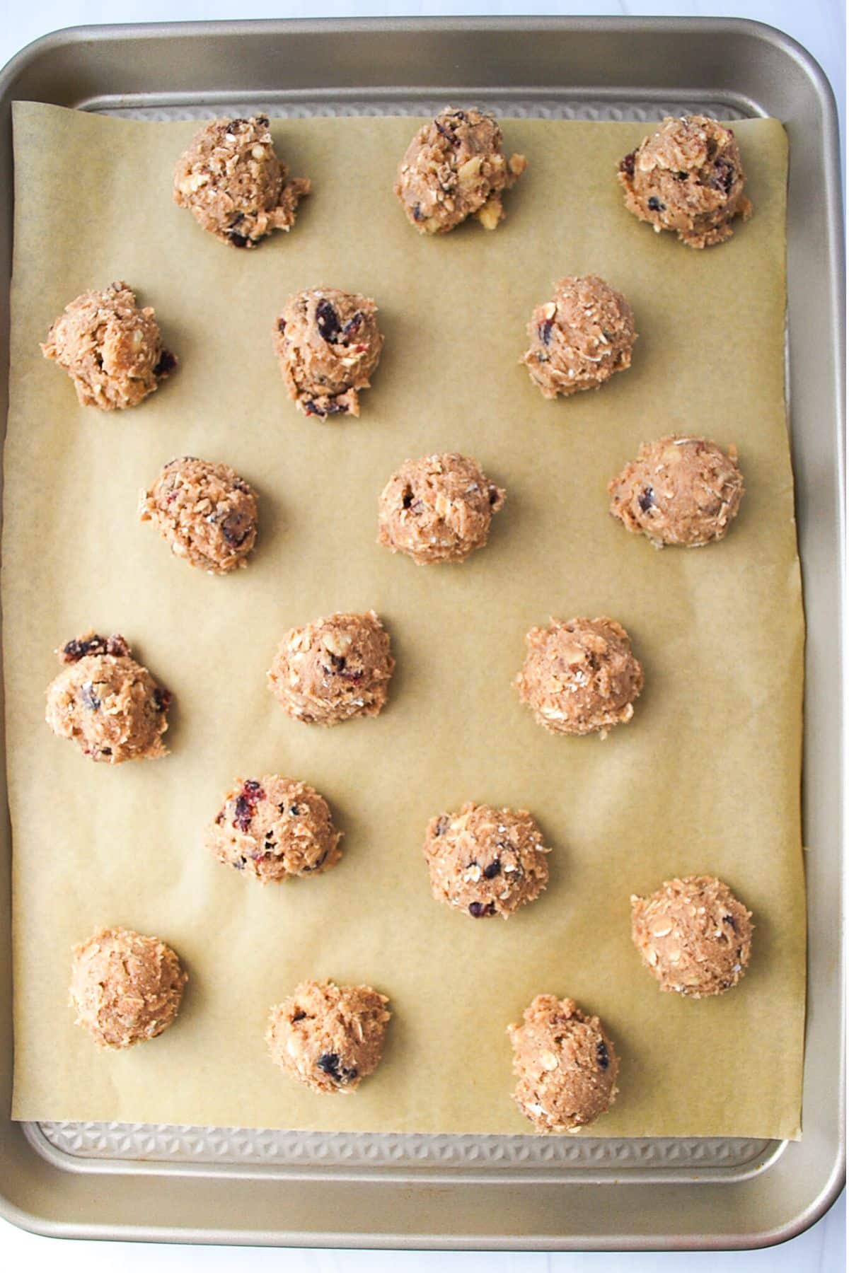 oatmeal cranberry cookie dough balls on a parchment lined baking sheet