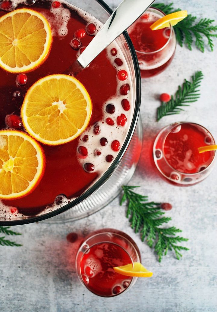 punch bowl with ladle and glasses of Christmas punch with greenery and cranberries in the background
