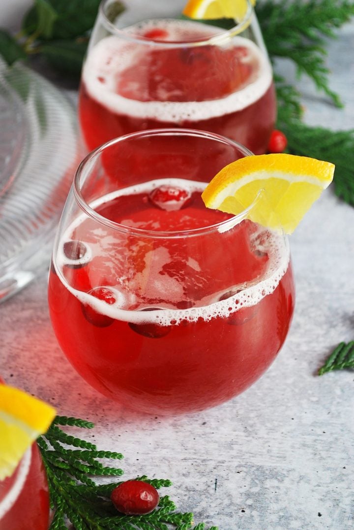 stemless wine glasses filled with cranberry Christmas punch with an orange slice on the rim